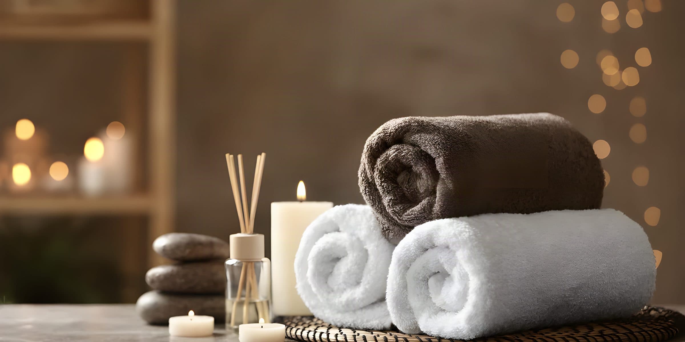 Gerollte Handtücher, Kerzen, Duftstäbchen und Massagesteine auf einem Tisch im Spa